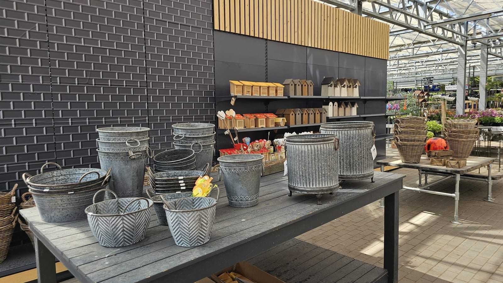 Zink-Übertöpfe und Körbe auf einem Präsentiertisch vor dunkler Holzwand
